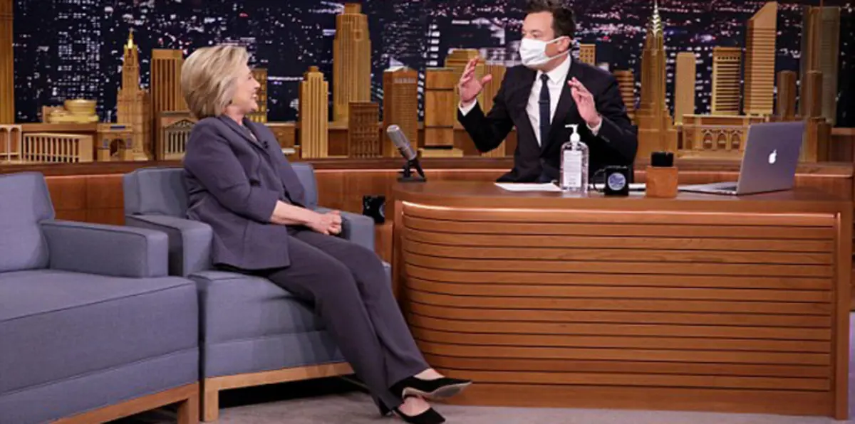 في أول ظهور بعد المرض..مذيع أمريكي يستقبل هيلاري كلينتون بكمامة ومطهّر (فيديو وصور)