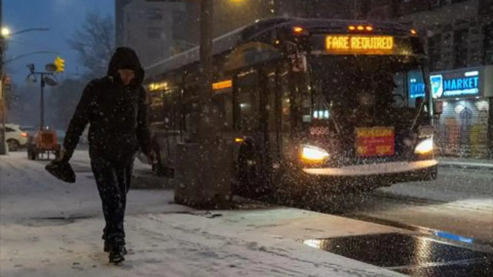 شخص يسير بجوار حافلة في أحد شوارع نيويورك خلال تساقط الثلوج