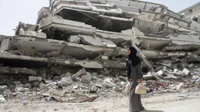 امرأة فلسطينية تحمل خبزًا تمر عبر أنقاض منزل دمر خلال حرب إسرائيل على قطاع غزة