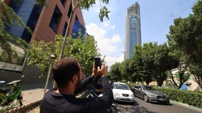 رجل يلتقط صورة لمبنى تضرر جراء غارة إسرائيلية على طهران