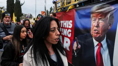 إسرائيليون بجانب لوحة تطالب ترامب بالعمل لإطلاق الرهائن