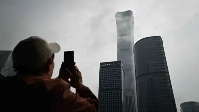 امرأة مسنة تستخدم هاتفها المحمول لالتقاط صور لناطحة سحاب تشاينا زون في منطقة الأعمال في بكين