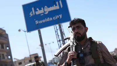 يقف أحد عناصر قوات الأمن السورية تحت لافتة في مدينة السويداء ذات الأغلبية الدرزية