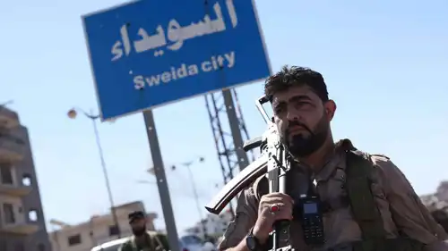 أحد أفراد قوات الأمن السورية تحت لافتة في مدينة السويداء