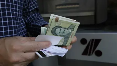 رجل يسحب أوراق نقدية بالريال الإيراني من ماكينة صرف آلي في العاصمة طهران