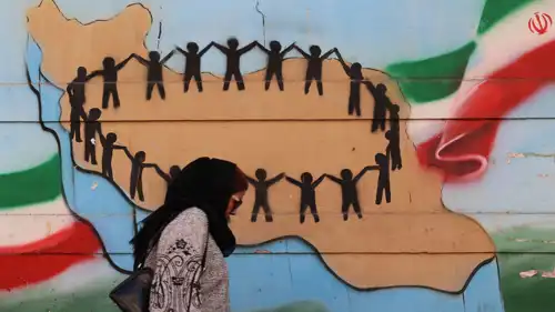 امرأة تمر أمام علم وخريطة إيران على جدار في طهران