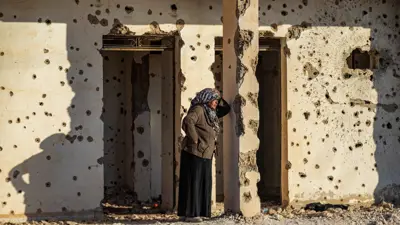 امرأة سورية، فارة من شمال حلب، متكئة على جدار مثقوب بالرصاص لدى وصولها إلى الطبقة، على المشارف الغربية للرقة