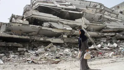 امرأة فلسطينية تمر عبر أنقاض منزل دمر خلال الحرب الإسرائيلية على غزة