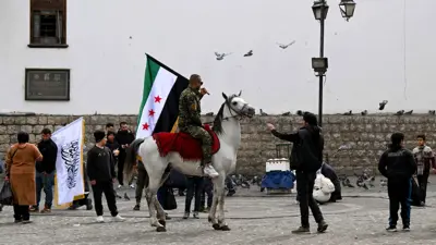 رجل يحمل العلم السوري الجديد وهو يمتطي جوادًا في سوق الحميدية بدمشق
