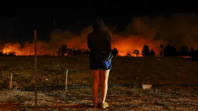 تقف امرأة بينما يكافح أفراد الطاقم لإطفاء حريق بالقرب من أوتو سنتر درايف في فينتورا، كاليفورنيا