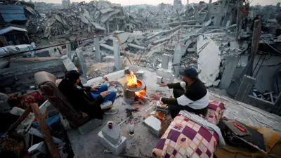فلسطينيون يجلسون بجوار النار بين أنقاض المباني المدمرة خلال الهجوم الإسرائيلي