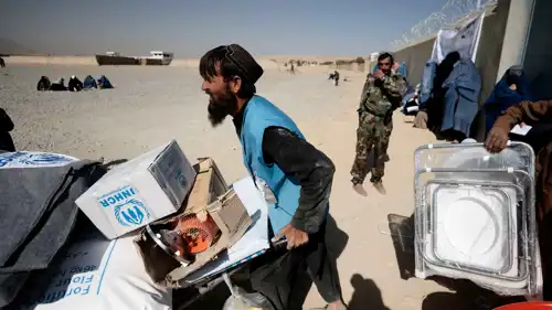 أحد موظفي المفوضية السامية للأمم المتحدة لشؤون اللاجئين يدفع عربة يدوية محملة بإمدادات إغاثة لعائلة أفغانية نازحة
