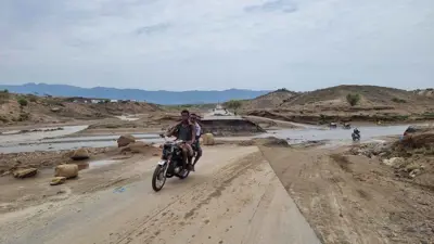 أشخاص يركبون دراجة نارية على طريق تضرر بسبب الفيضانات في أعقاب الأمطار الغزيرة باليمن