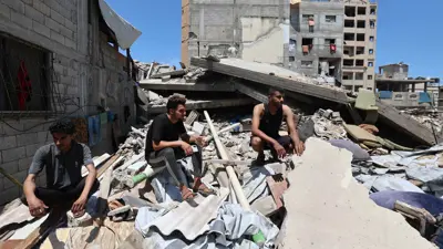 فلسطينيون من غزة يجلسون فوق مبنى مهدم