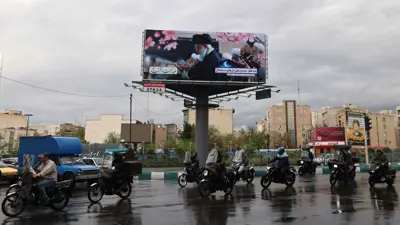 يمر الركاب أمام لافتة تحمل صورة خامنئي