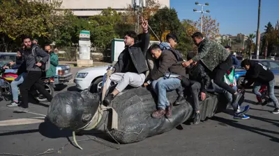 سوريون فوق تمثال لحافظ الأسد بعد تدميره