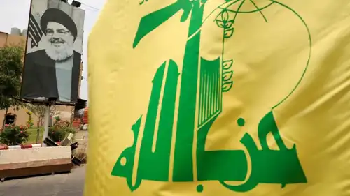 علم حزب الله بجانب صورة لأمين عام الحزب الراحل نصر الله.