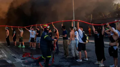 متطوعون ورجال إطفاء يحاولون إطفاء حريق في مبنى أثناء اندلاع حريق غابات