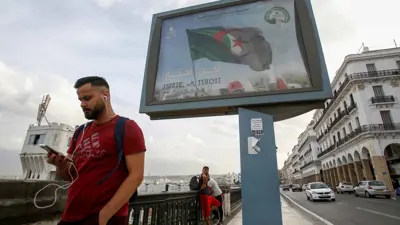 رجل يمر أمام لوحة إعلانية لحملة انتخابية رئاسية سابقة في الجزائر