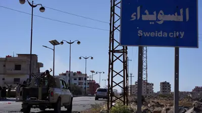قوات الأمن السورية تتجمع بالقرب من لافتة طريق مكتوب عليها "مدينة السويداء"
