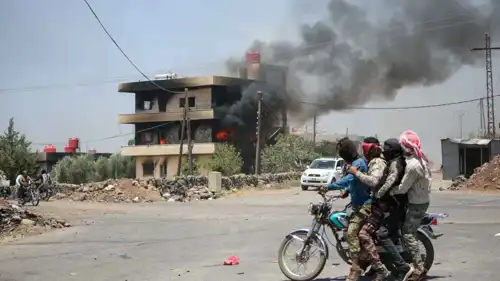 مقاتلون من العشائر ينظروف إلى منزل تم إحراقه في السويداء