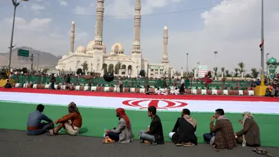 حوثيون يجلسون بجوار علم إيران