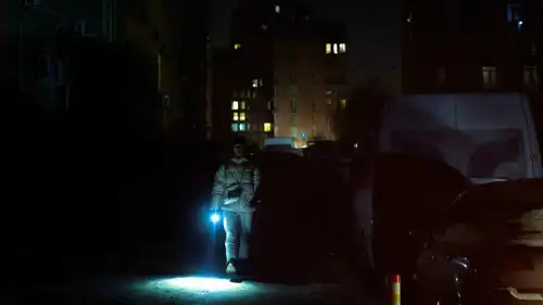رجل يحمل مصباحًا يدويًا بحيٍّ انقطعت عنه الكهرباء بعد غارات روسية حديثة على كييف