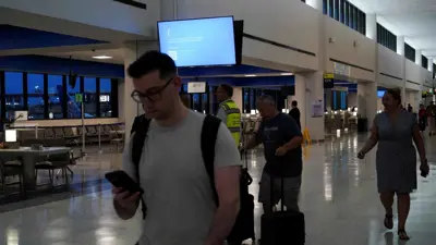 مسافرون يمرون بجانب شاشة عرض معطلة داخل مطار نيوارك الدولي في ولاية نيوجيرسي الأمريكية