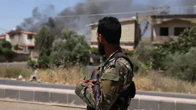 عنصر من الأمن السوري ينظر نحو منزل يحترق قرب السويداء