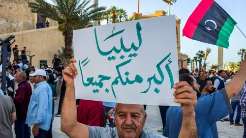 رجل يحمل لافتة في احتجاج مناهض للحكومة، في ساحة الشهداء بالعاصمة الليبية طرابلس