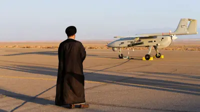 مسؤول إيراني يقف أمام مسيّرة خلال مناورة عسكرية